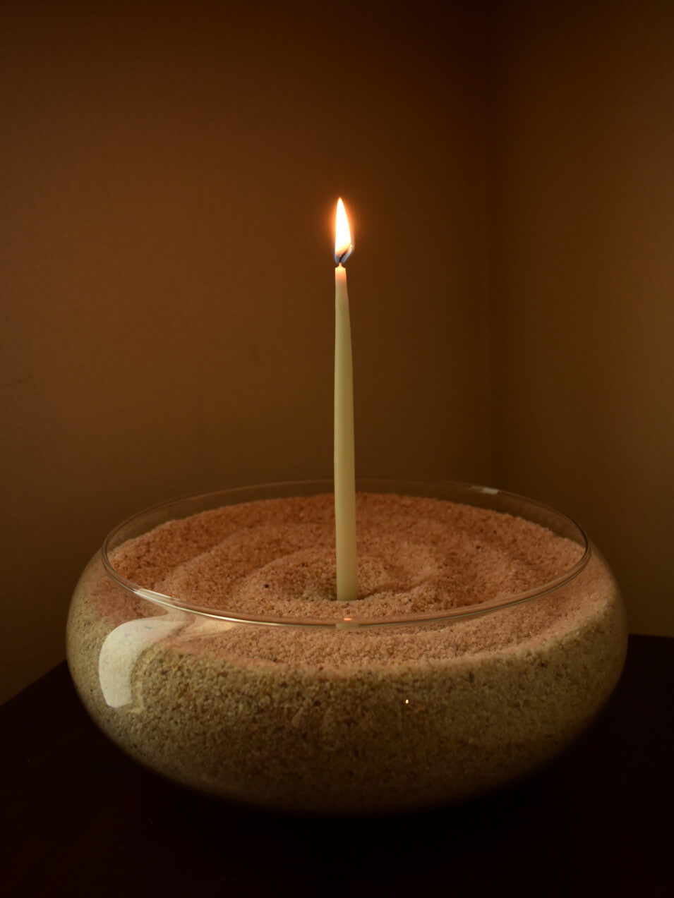 Glowing candle in a bowl of sand.